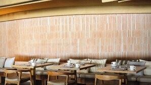 Un restaurant amb taules i cadires de fusta, coixins amb ratlles i una paret de maó.