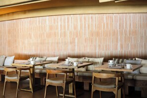 A restaurant with wooden tables and chairs, striped cushions, and a brick wall.