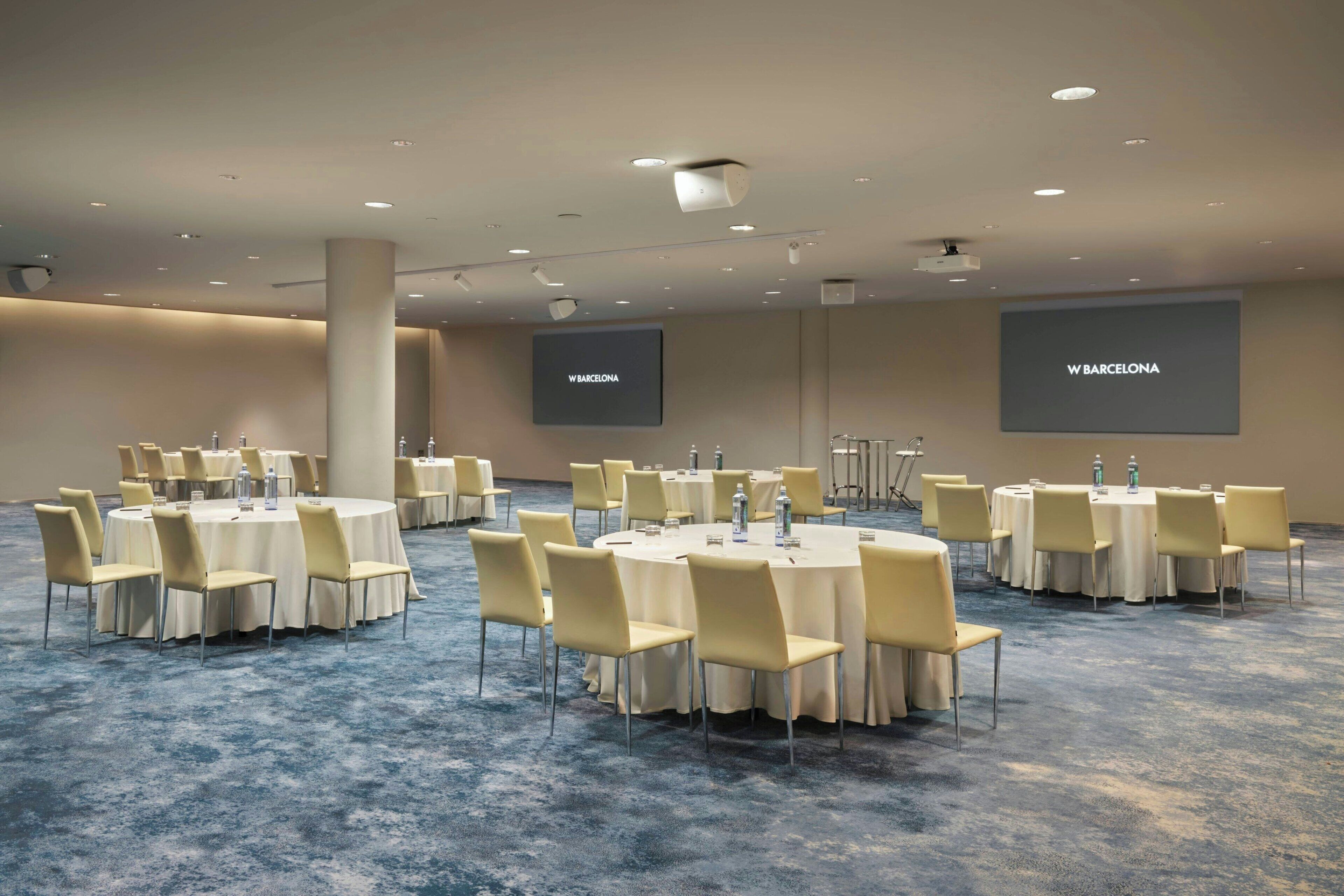 Un salón de conferencias con mesas redondas, sillas y suelo alfombrado.