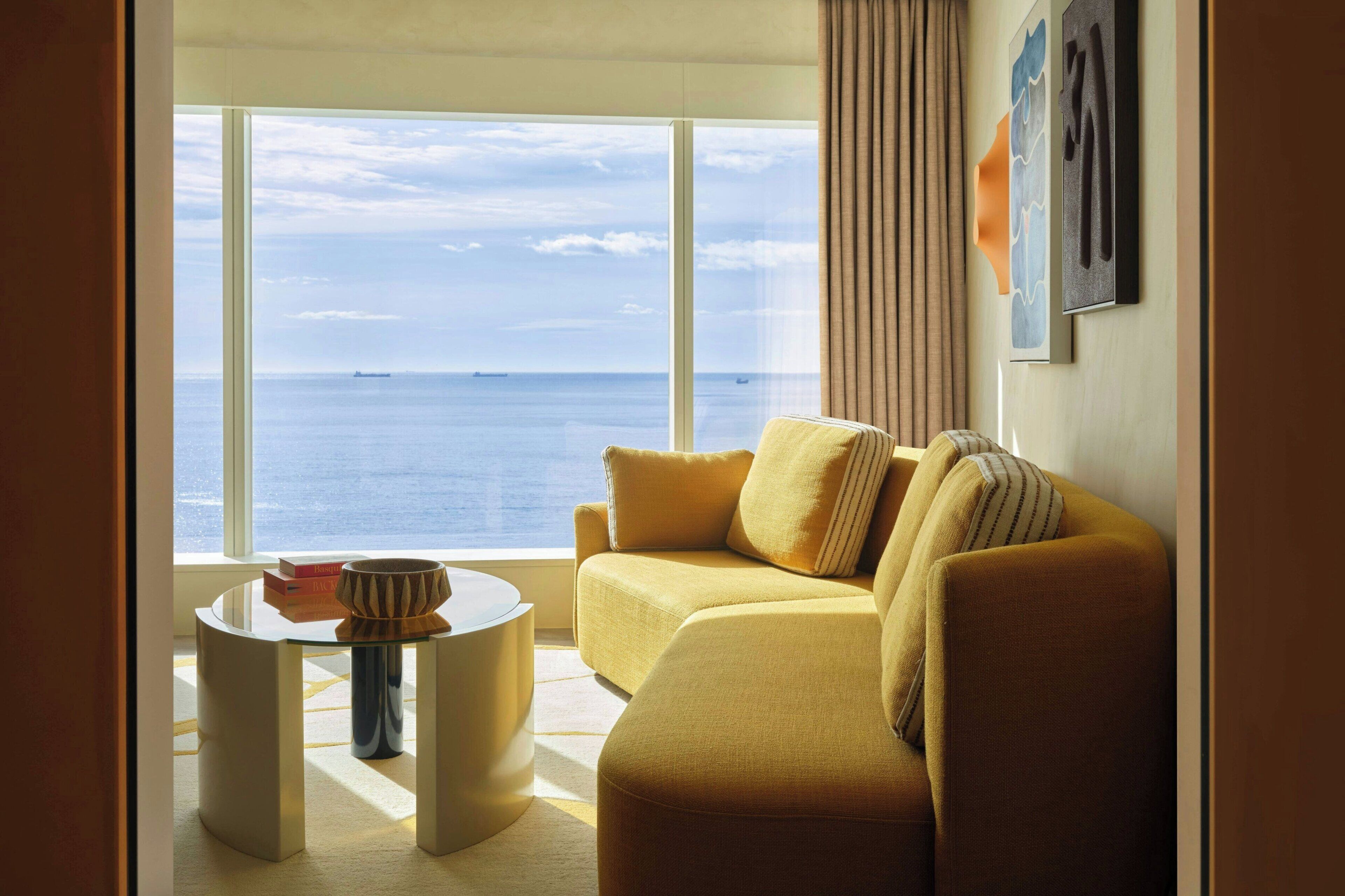 Un salón moderno con un sofá, una mesita redonda y vistas al mar.