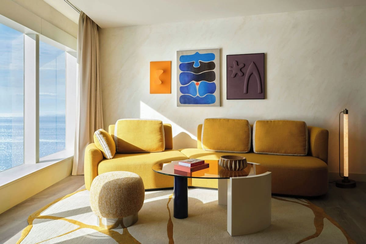 Uma sala de estar moderna com sofá, banquinho, mesa de centro e arte na parede.
