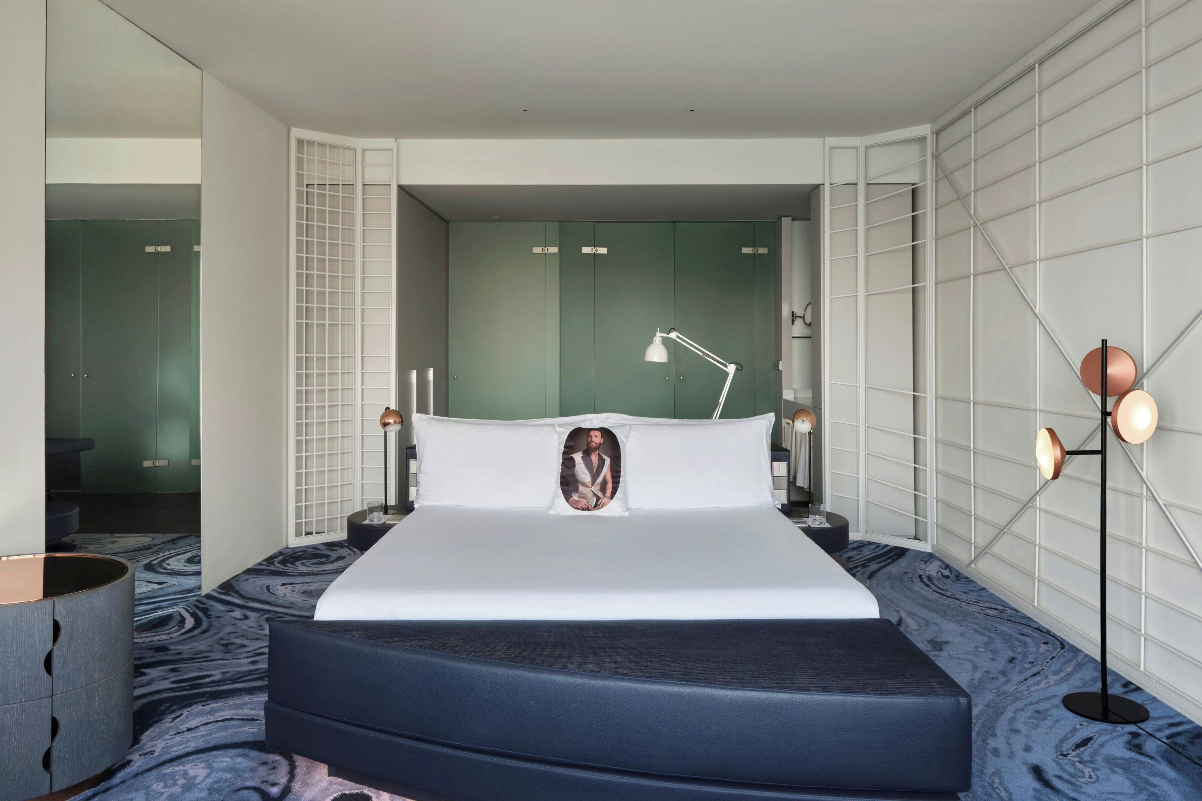 Habitación de hotel moderna con una cama grande, una lámpara de noche, una mesita de noche y una lámpara de pie.