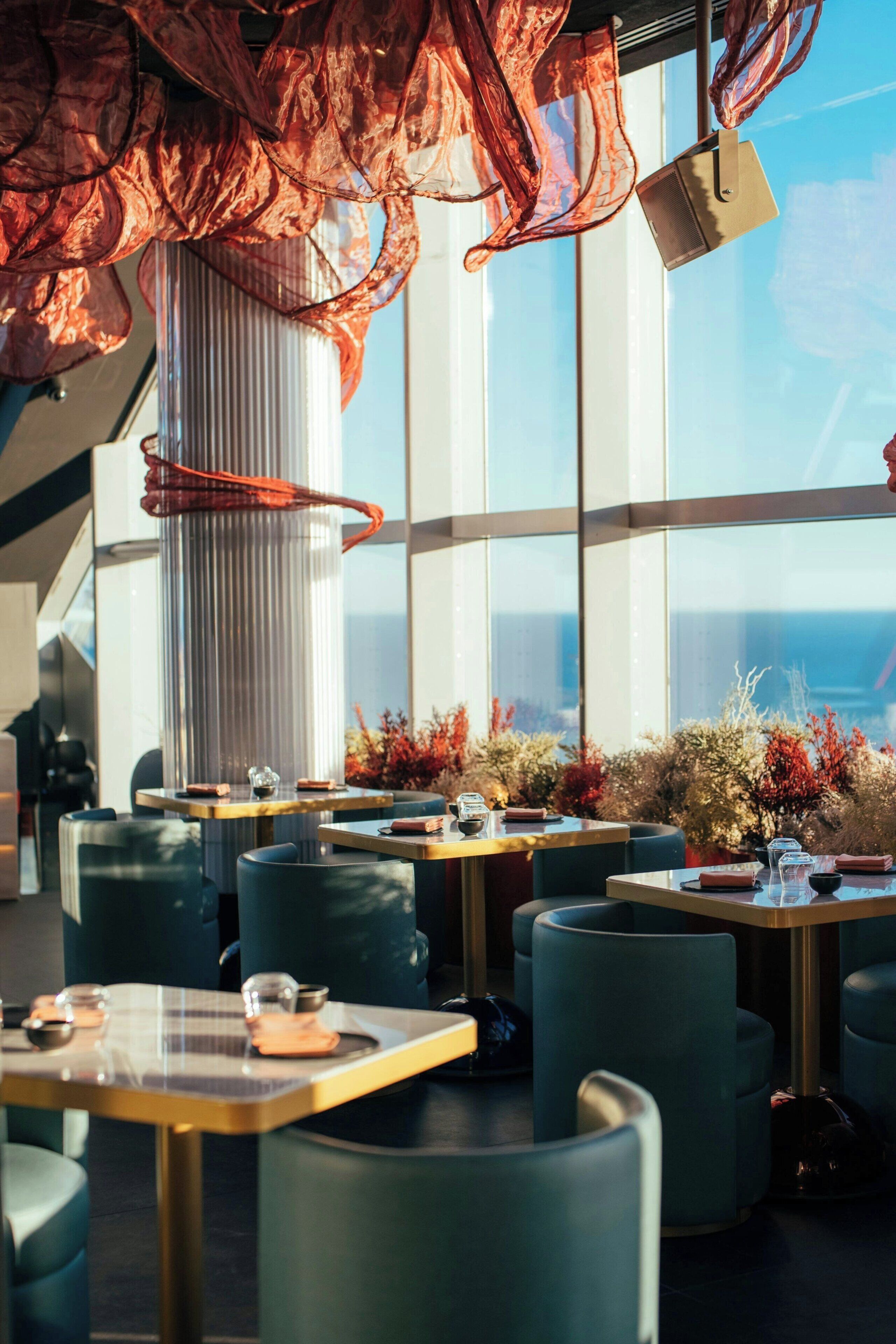 Un comedor moderno con mesas y sillas, ventanas amplias y vistas a la ciudad.