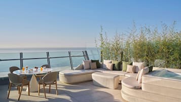 A terrace with a dining table, chairs, a sofa, and a hot tub, overlooking the sea.