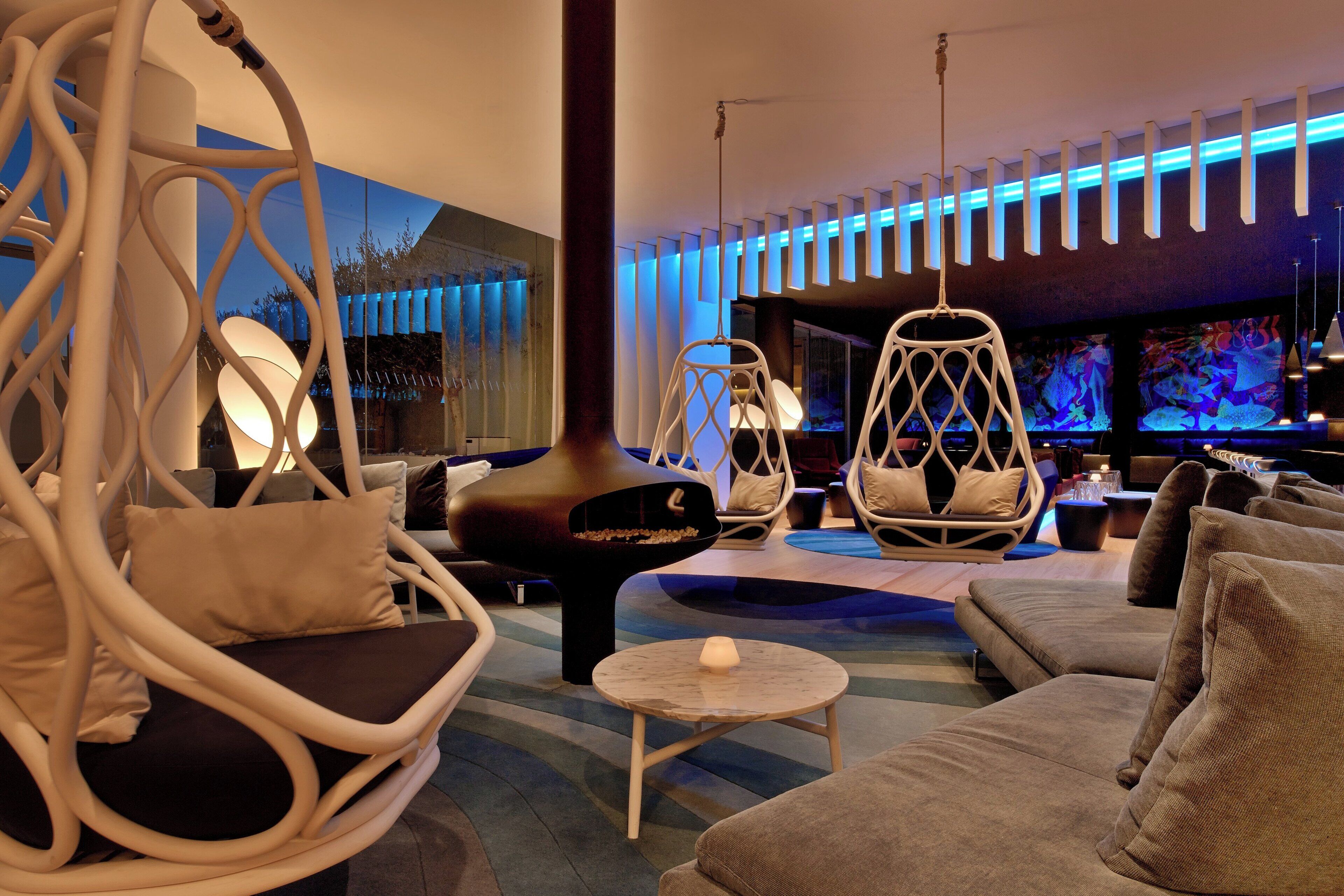 Un moderno salón con diferentes disposiciones de asientos, incluyendo un sofá, dos sillones y un sillón colgante. Hay una pantalla de televisión que muestra una escena submarina.