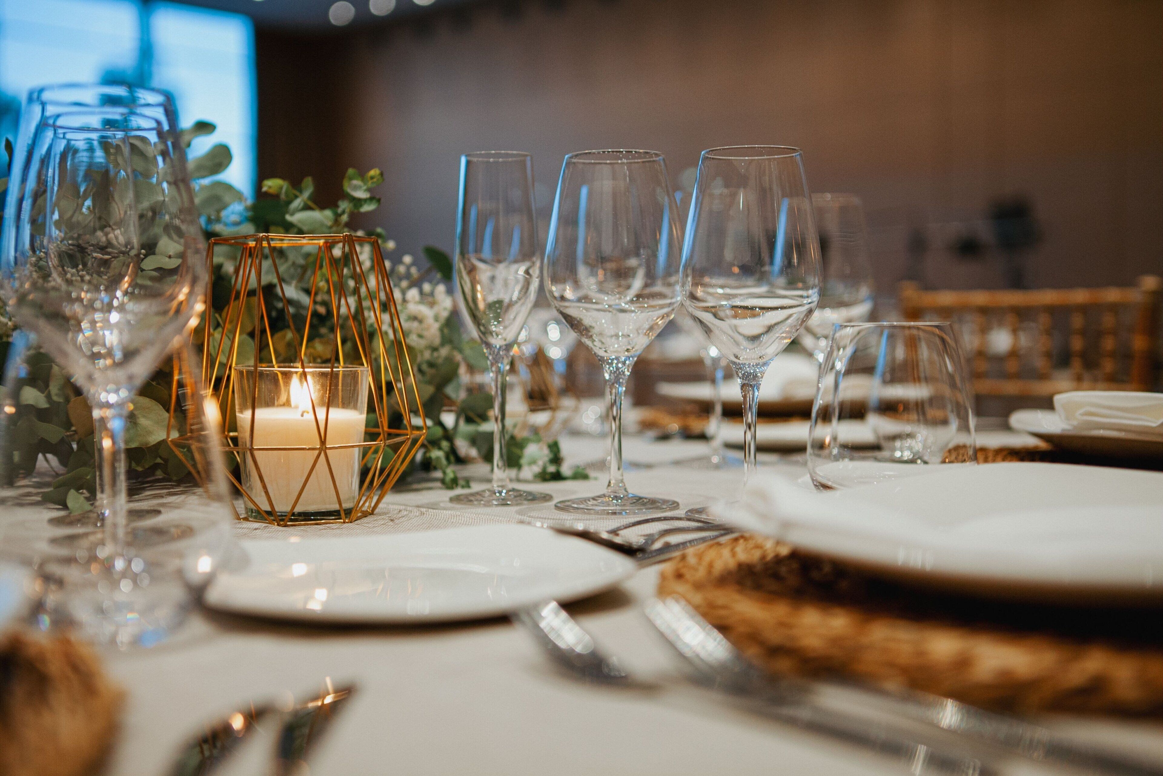 Una mesa dispuesta para una cena formal, con copas de vino, platos y una vela en un candelabro de vidrio geométrico.
