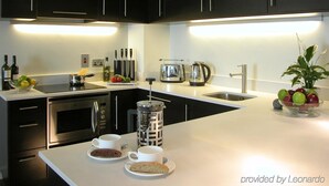 A modern kitchen with black cabinets, a stainless steel oven, a kettle, and a coffee maker. There are plates with cookies and cups on the counter. - Atelier EC1 by Bridgestreet (London)