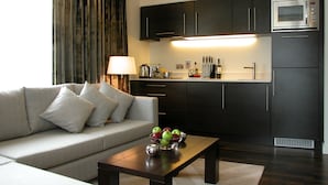 A modern living room with a sofa, a coffee table with fruit, and a kitchen area with dark cabinets and a microwave. - Atelier EC1 by Bridgestreet (London)