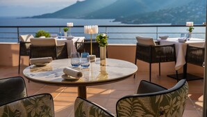 A terrace with round tables, chairs, and a view of the sea and mountains. - Tiara Yaktsa Côte d'Azur (Theoule-sur-Mer)