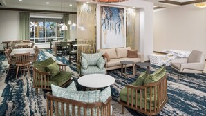 A hotel lobby with a large seating area, a dining section, and a large window providing a view of the outside. - Fairfield Inn & Suites by Marriott Orlando at SeaWorld (Orlando)