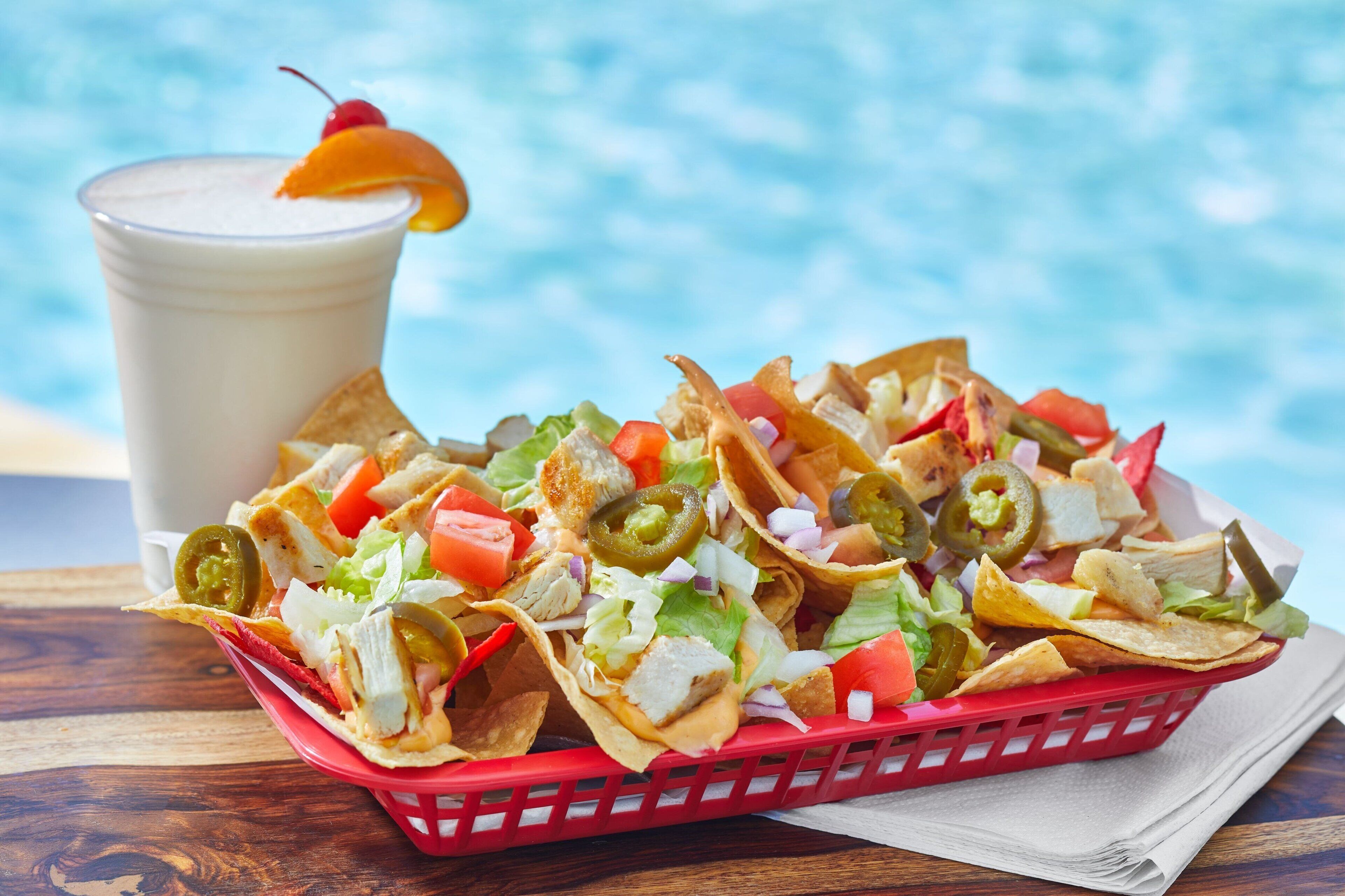 Nachos with toppings and a drink in a red basket.