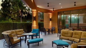 An outdoor seating area with yellow sofas and blue cushions, surrounded by glass walls and a view of greenery. - Fairfield Inn & Suites by Marriott Orlando at SeaWorld (Orlando)