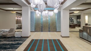 A modern hotel lobby with a central seating area, a reception desk, and a decorative wall with hanging lights. - Fairfield Inn & Suites by Marriott Orlando at SeaWorld (Orlando)