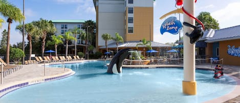 A swimming pool with a penguin sculpture, lounge chairs, and a building with a sign reading "Splash Zone".