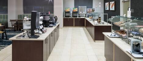 A modern hotel lobby with a central counter, seating area, and a coffee station.