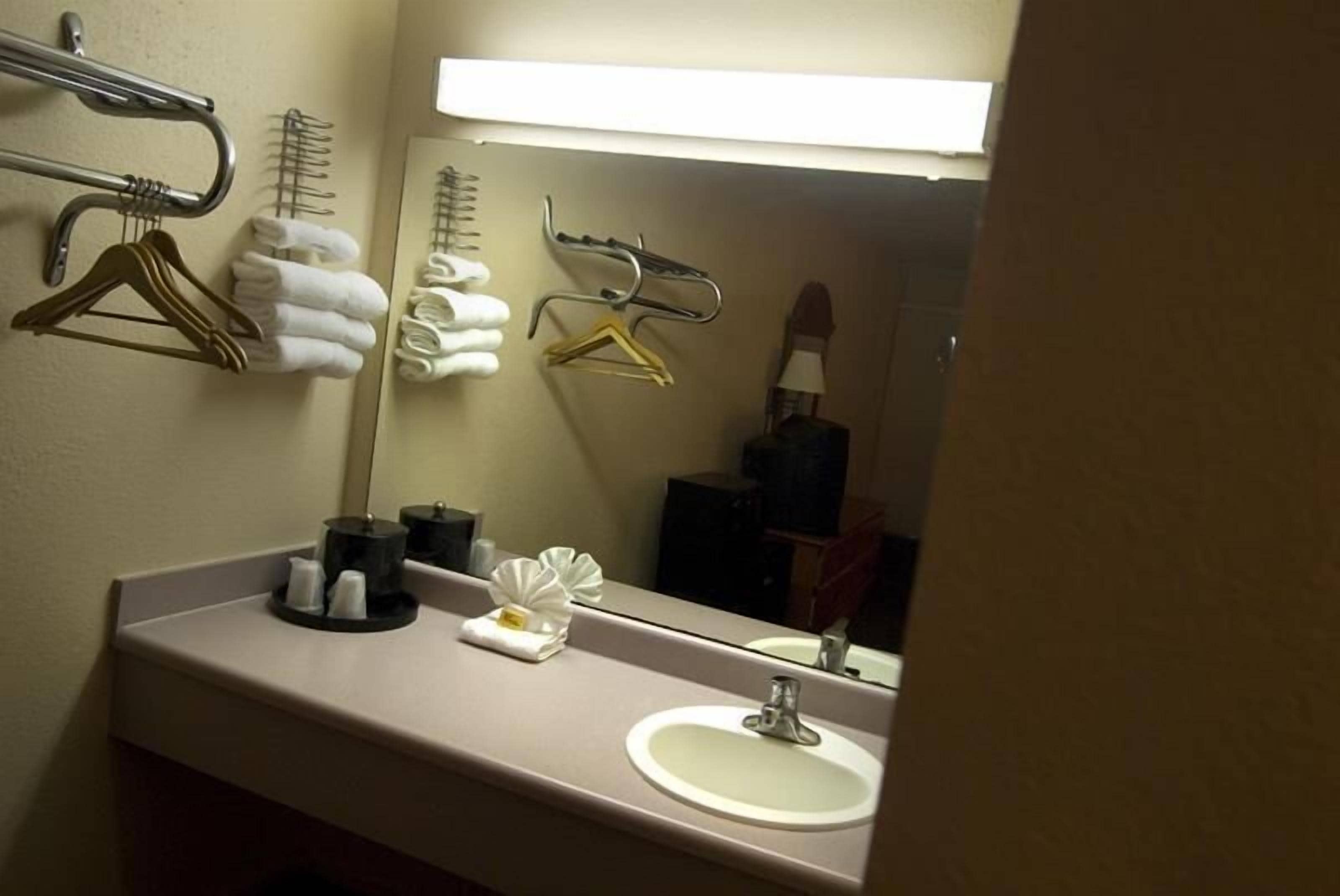 Un baño de hotel con lavamanos, espejo, toallero y ropa colgada.