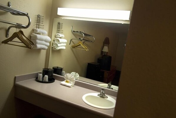 A hotel bathroom with a sink, mirror, towel rack, and hanging clothes. - Budget Inn Sanford (Sanford)