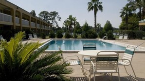 A swimming pool with lounge chairs and a table, surrounded by palm trees and a building with balconies. - Budget Inn Sanford (Sanford)