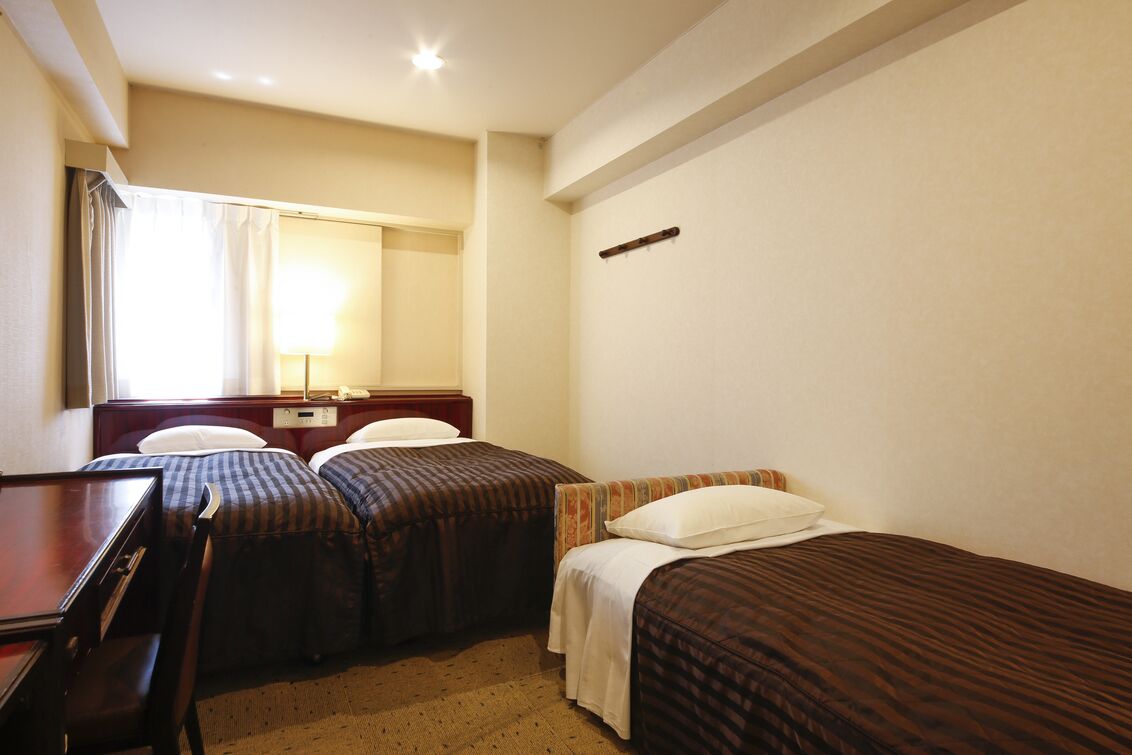 A hotel room with two single beds, a desk, a chair, a mirror, and a window with curtains.