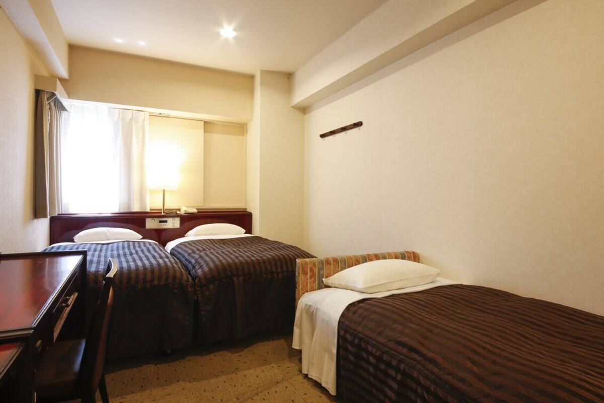 A hotel room with two single beds, a desk, a chair, a mirror, and a window with curtains.
