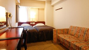A hotel room with a wooden desk, two beds with striped bedding, a sofa, a mirror, and a lamp. - Hotel Sunlife (Osaka)