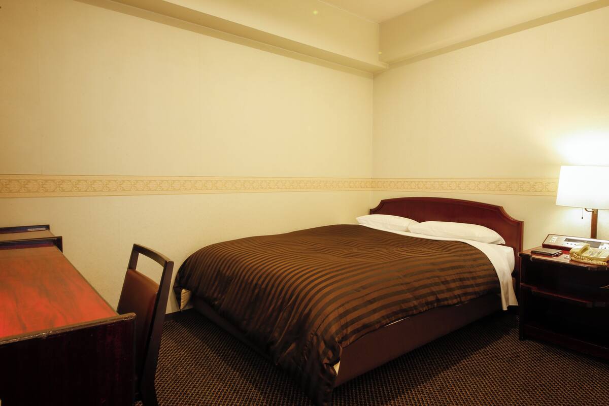 A hotel room with a bed, a desk, and a nightstand with a lamp.