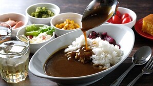 A bowl of rice with a brown sauce being poured over it, accompanied by various side dishes. - Hotel Sunlife (Osaka)