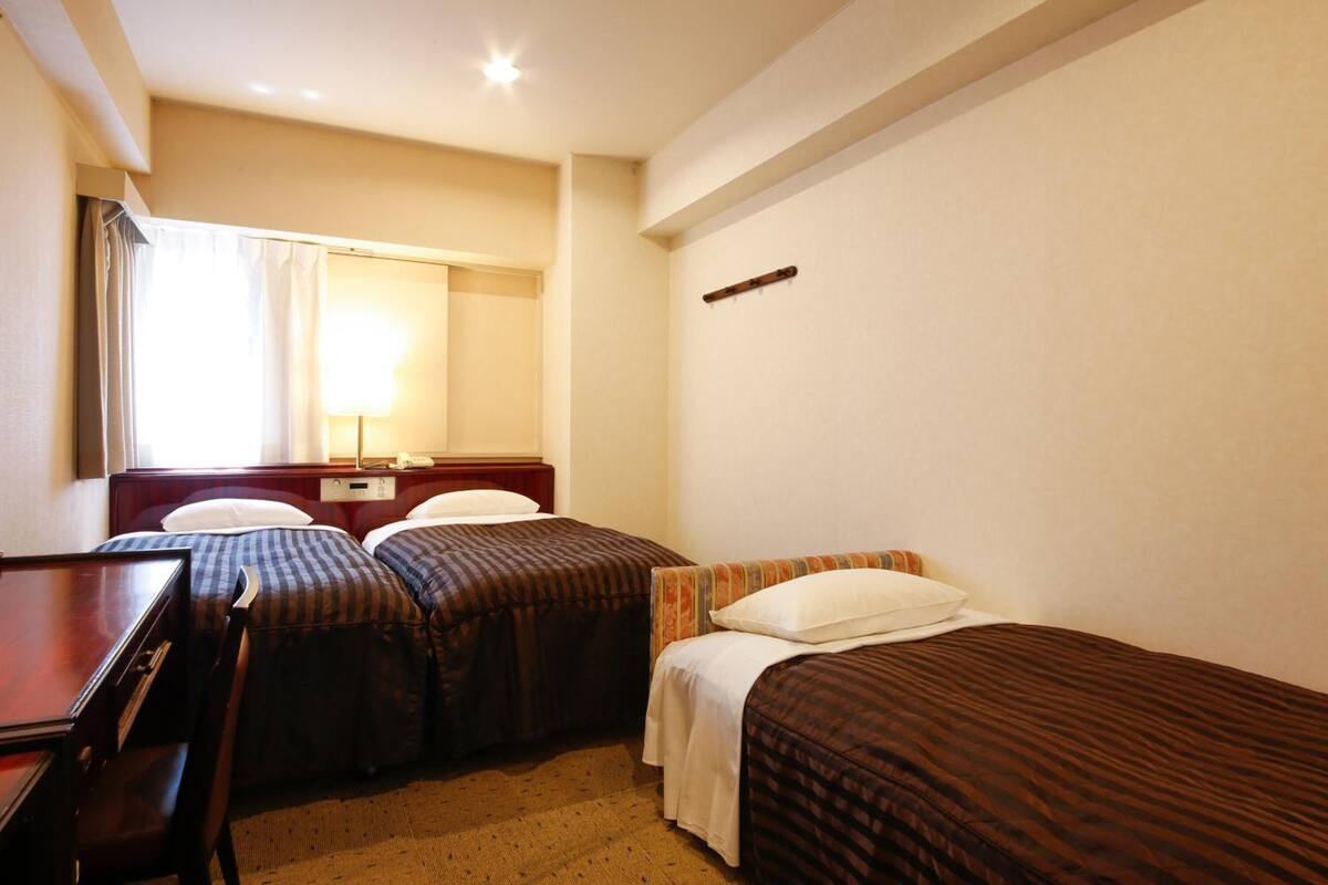 A hotel room with two single beds, a desk, and a chair.