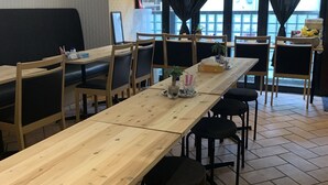 A restaurant interior with wooden tables and black cushioned booths, a large banner reading "Produced by Kitchen J", and a view of the outside through large windows. - Hotel Sunlife (Osaka)