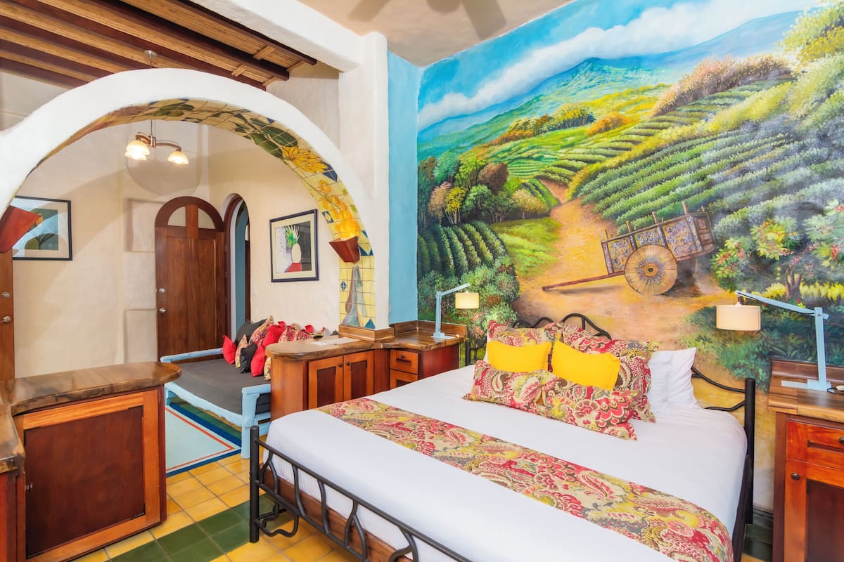 A bedroom with a bed, wooden furniture, a mural of a landscape, and a tiled floor.