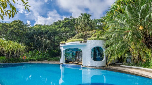 A clear blue swimming pool with a white structure featuring a circular window and a small roof.
