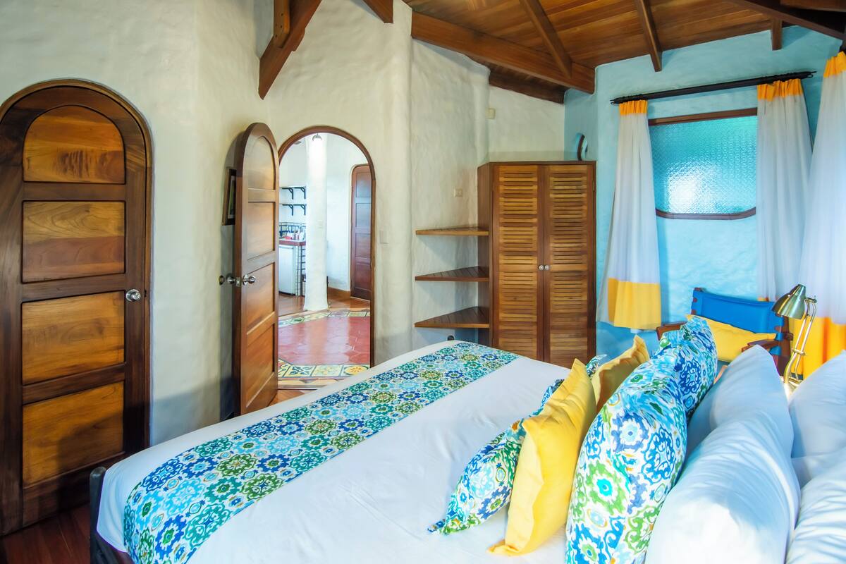 A bedroom with a bed, wooden wardrobe, and a window with curtains.