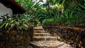 A stone staircase surrounded by lush greenery, leading to a building with a red roof.