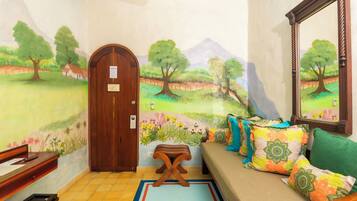 A room with a mural of a landscape, a wooden door, a bench, a sofa with colorful cushions, and a mirror on the wall.