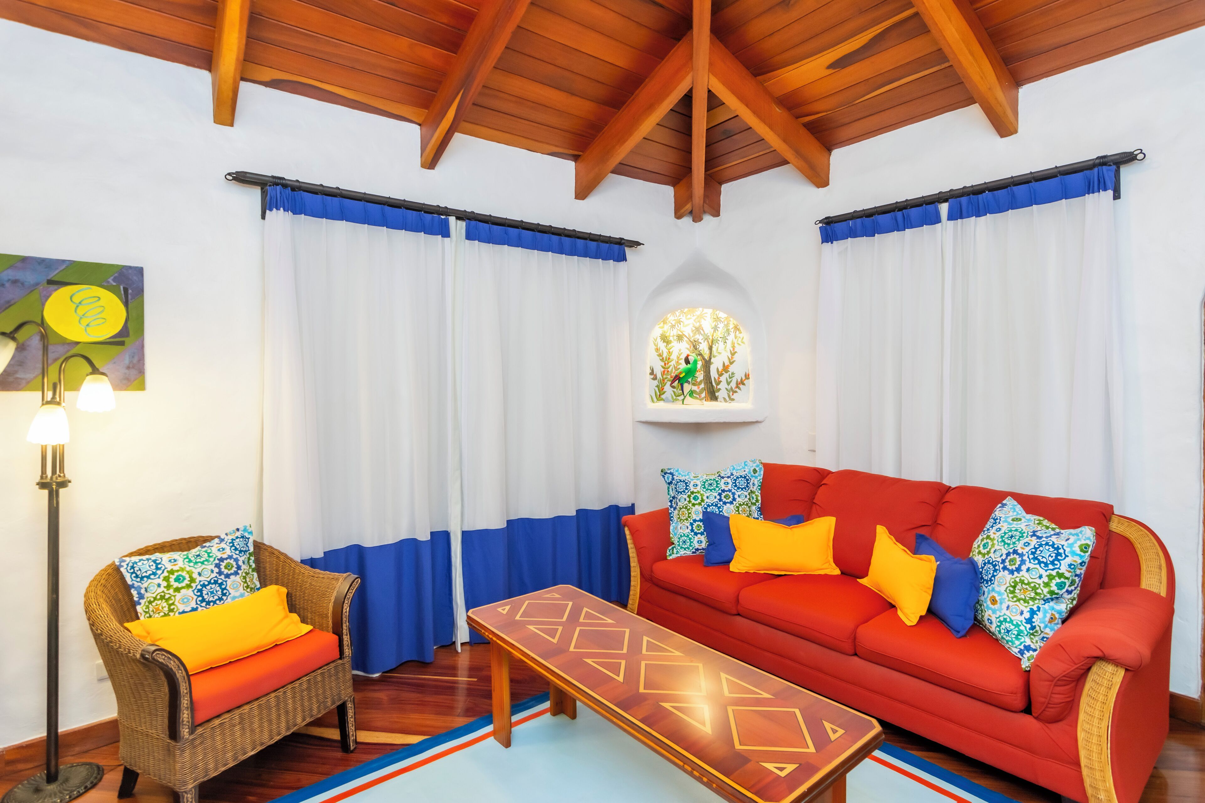 A room with a red sofa, wicker chair, and a wooden coffee table.