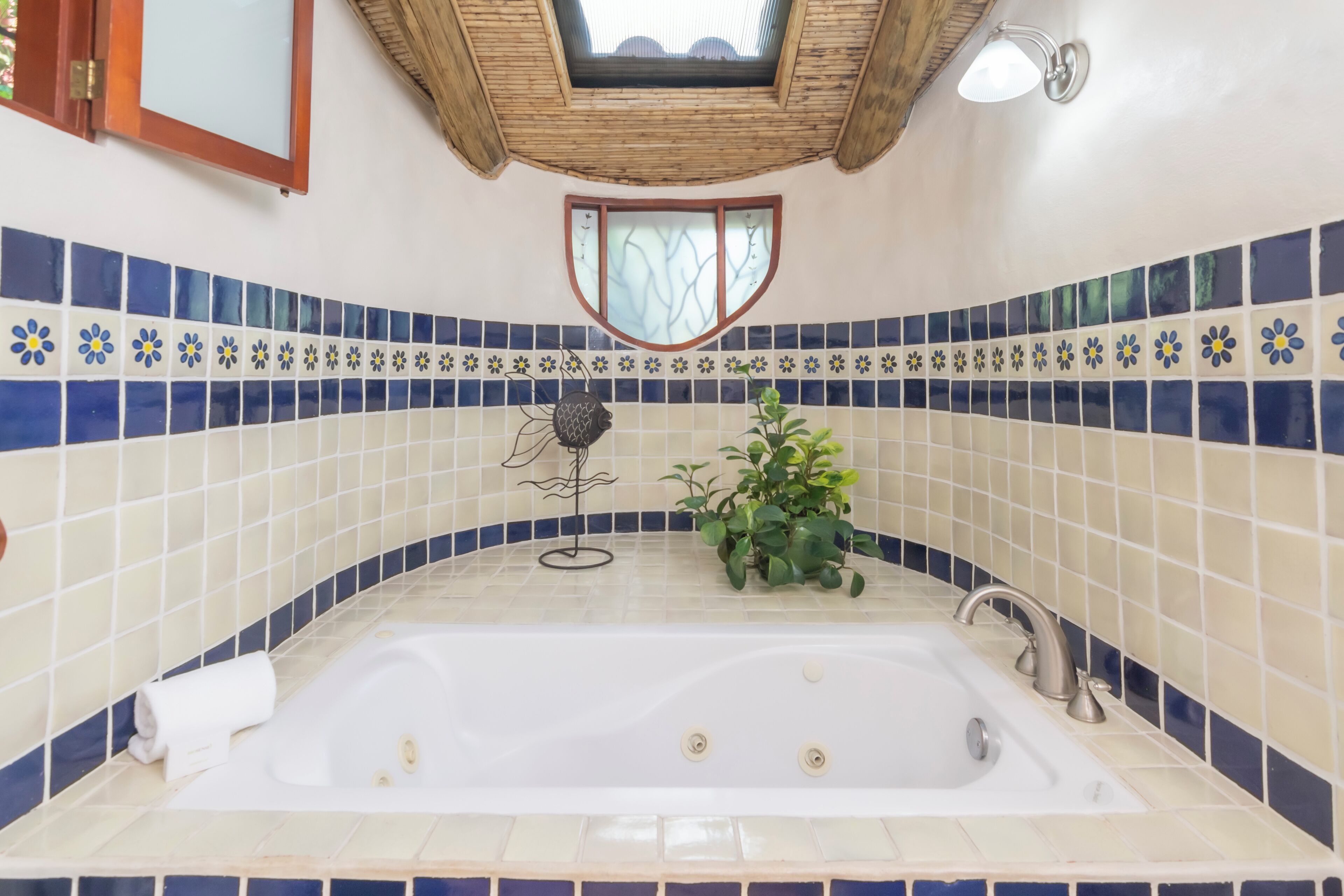 A bathroom with a bathtub, a towel, a potted plant, and a decorative window.
