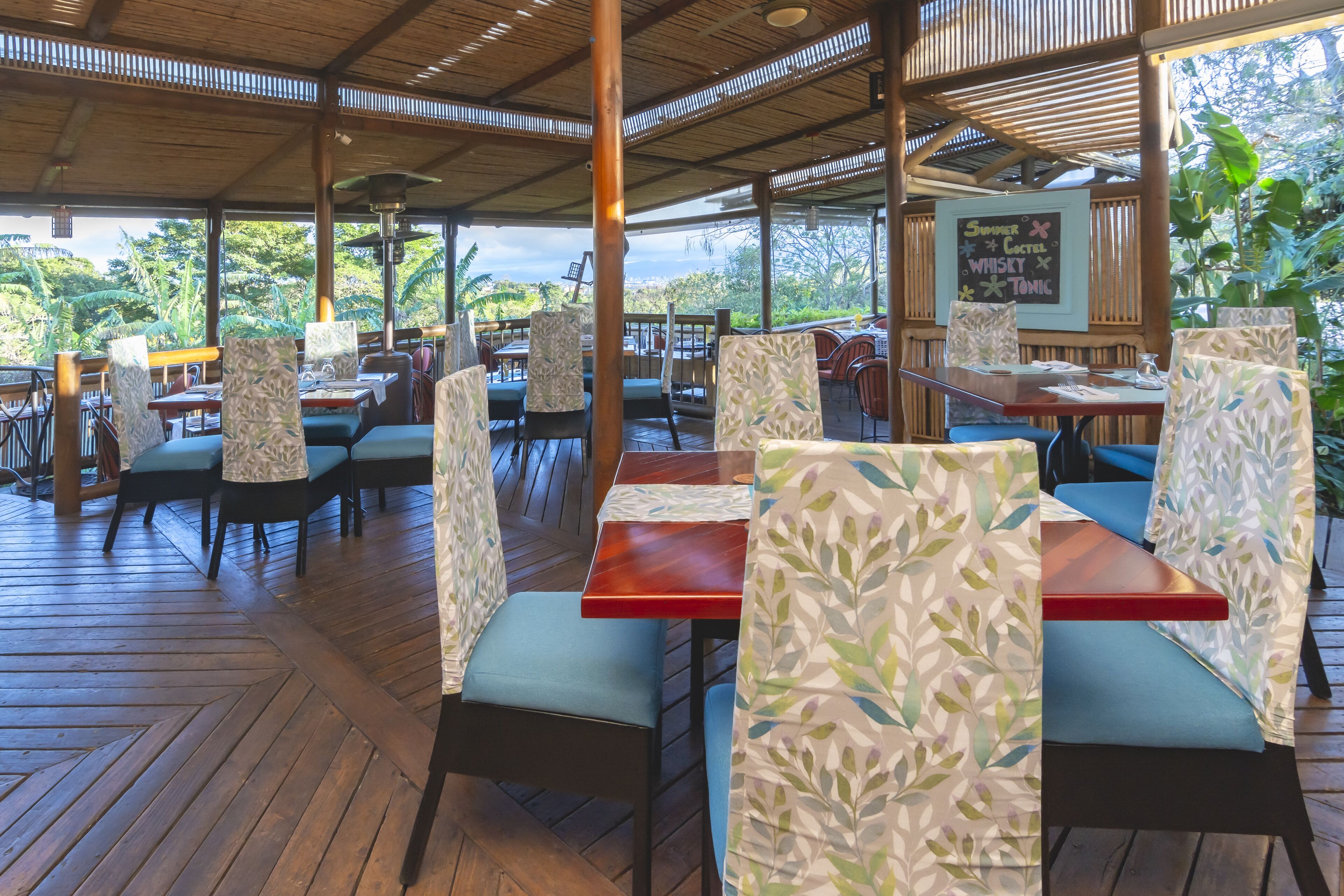 Un restaurant en plein air avec des tables et des chaises en bois, abrité par un toit en bambou et entouré d’une végétation luxuriante.