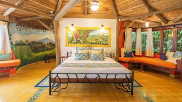 Relax in a spacious room with a high ceiling, featuring a large bed, vibrant mural, and seating area with a view.