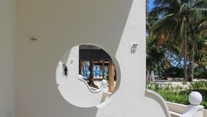 Una ventana circular con vista a un área de piscina, palmeras y un edificio de fachada blanca.