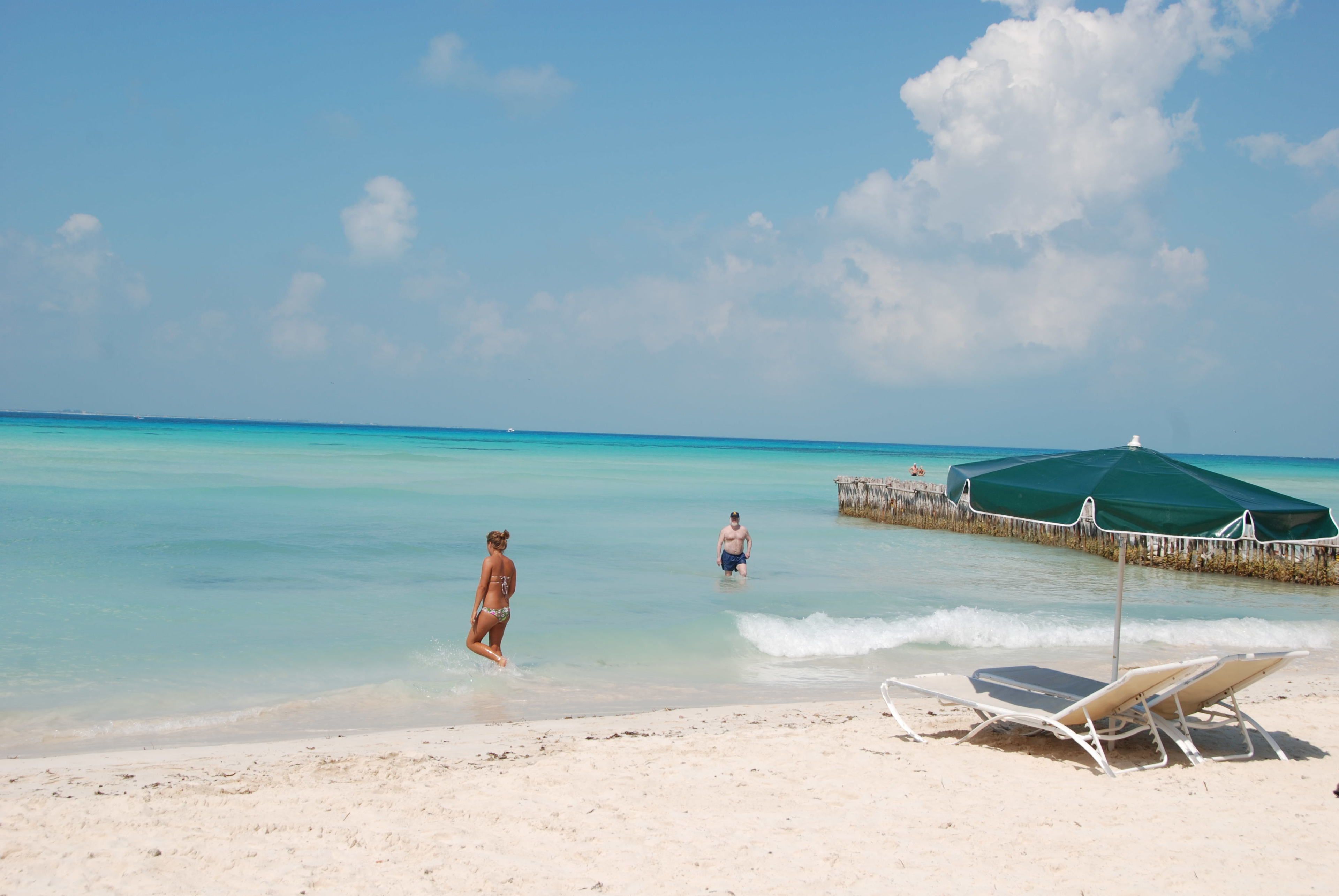 A beach with clear turquoise water, a sandy shore, and a few beach chairs and umbrellas.