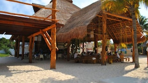 Una estructura en la playa con techo de paja, vigas de madera y suelo arenoso.
