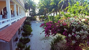 Un hotel con un paseo techado, palmeras y flores de buganvilla.