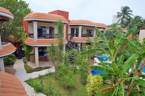 A resort with multiple buildings featuring red-tiled roofs and balconies, surrounded by lush greenery and palm trees.