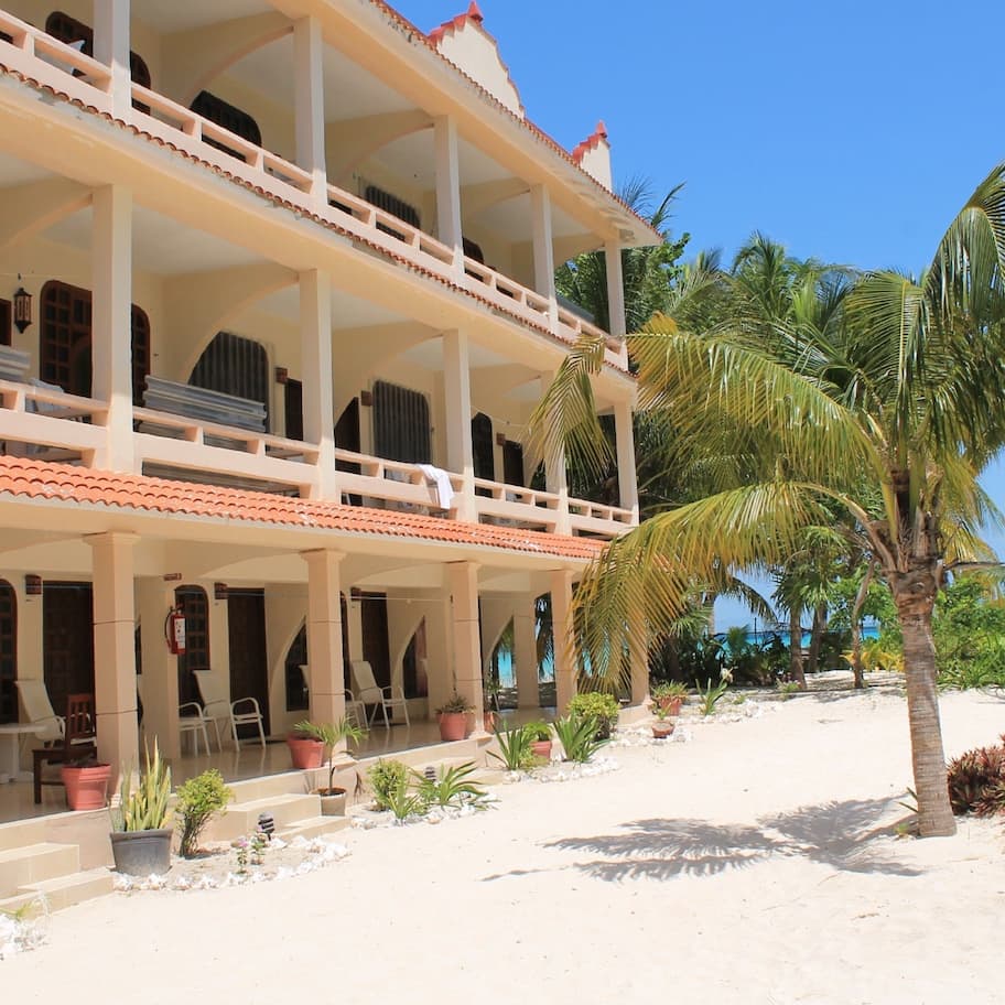 A two-story building with balconies, potted plants, and a sandy beach area.
