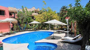 Una piscina con sillones de descanso y sombrillas, rodeada de edificios y árboles.