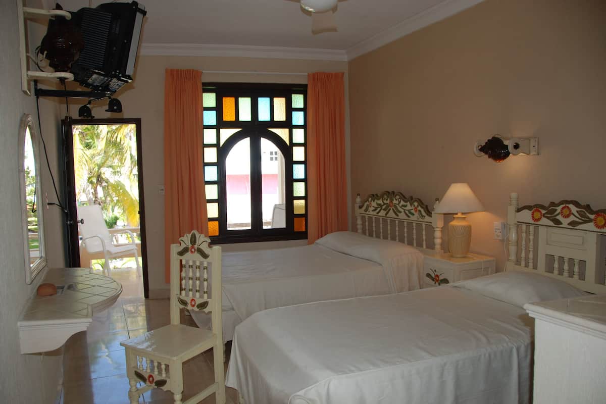A hotel room with two beds, a small table, a chair, a TV, and a window with curtains.