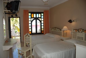 A hotel room with two beds, a small table, a chair, a TV, and a window with curtains.