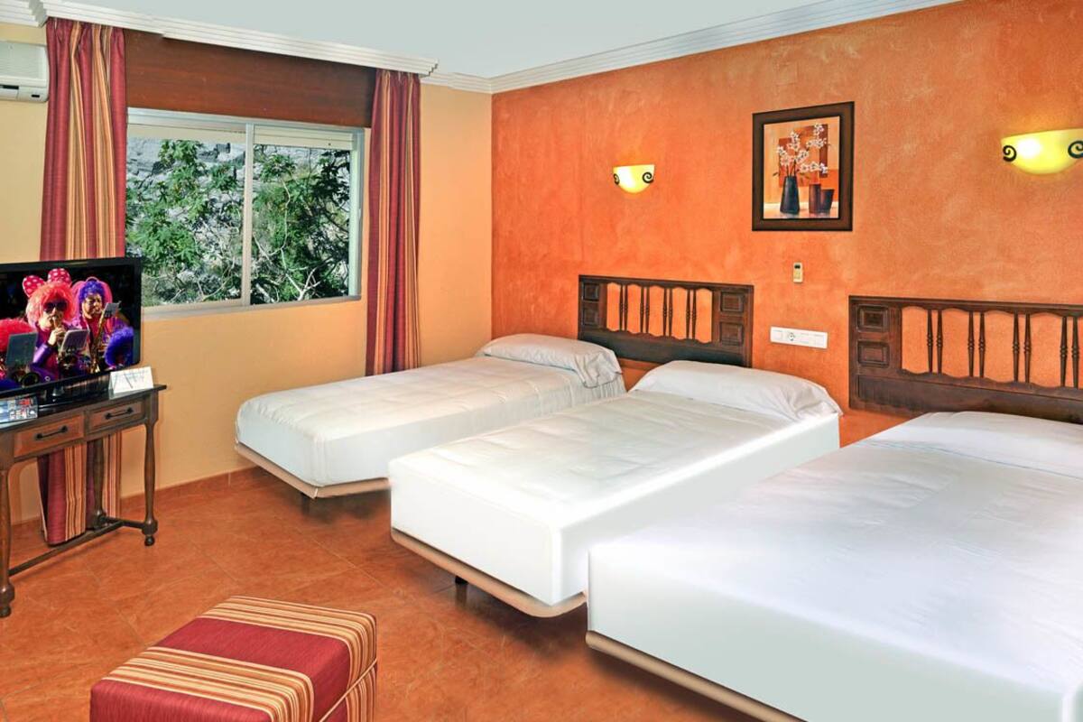 A hotel room with two single beds, a TV, a desk, and a window with curtains.