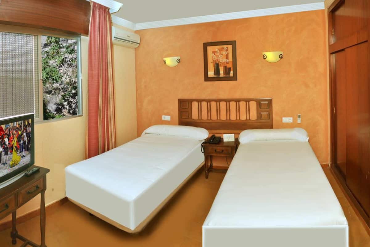 A hotel room with two single beds, a TV, a wooden nightstand, and a window with curtains.