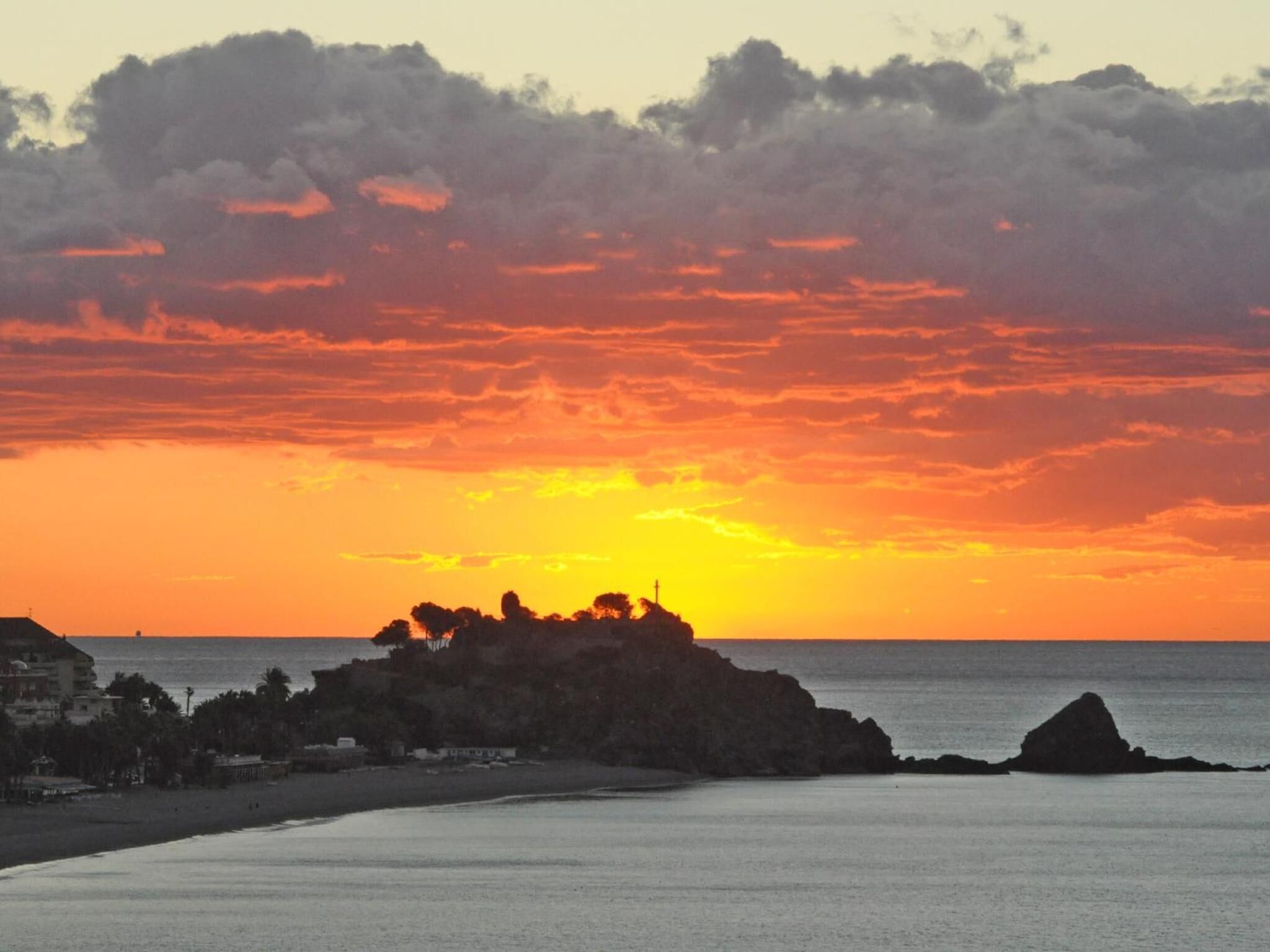 A sunset over a coastal landscape with rocky formations and a beach.